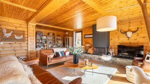 A cozy log cabin interior with a fireplace, leather furniture, and a bookshelf.