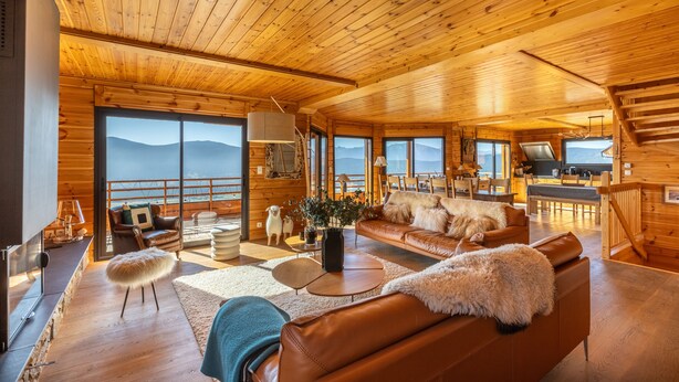A spacious wooden cabin with a large living area, a dining area, and a balcony with mountain views.