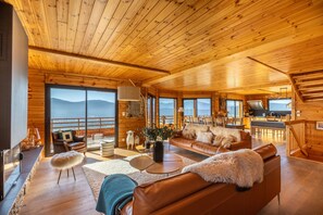 Une cabane en bois spacieuse, dotée d’un grand salon, d’un coin repas et d’un balcon offrant une vue sur les montagnes.