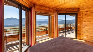 A wooden cabin with large windows offering a view of a mountainous landscape.