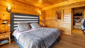 A wooden cabin bedroom with a bed, bedside lamps, and a closet.