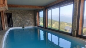 A large indoor swimming pool with stone walls and large windows offering a view of the mountains.