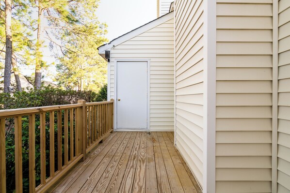 A wooden deck with a white door, surrounded by greenery and trees.