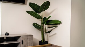 Ein Zimmer mit einem Holzbüro, einer schwarzen Pflanze im schwarzen Topf und einem kleinen Tisch mit einem farbenfrohen Gegenstand darauf.
