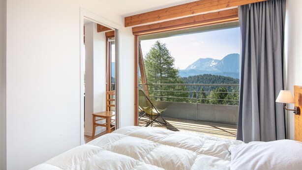 A bedroom with a large bed, a chair, and a balcony with a mountain view. - Le Machu - Appt 3*, vue montagne (Chamrousse)
