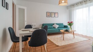 A modern living room with a dining area, a green sofa, a coffee table, and a hanging light fixture.