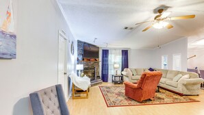 Un salón espacioso con chimenea, un sofá grande, un sillón rojo y un ventilador de techo.