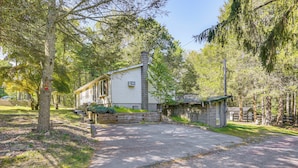 A single-story house with a chimney, surrounded by trees and a gravel driveway.