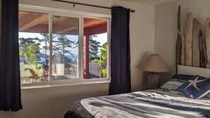 A bedroom with a bed, a window with curtains, a lamp, and a wall with wooden decor. - Cozy 2-bedroom, coastal inspired, suite with AC in beautiful Campbell River (Campbell River)