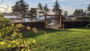 A backyard with a grassy lawn, a wooden deck, and a view of trees and a body of water. - Cozy 2-bedroom, coastal inspired, suite with AC in beautiful Campbell River (Campbell River)