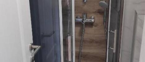 A glass-enclosed shower stall with a wooden floor, a showerhead, and a handheld shower attachment.