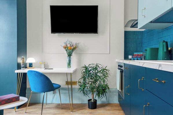 Eine moderne Küche mit Fernseher, einem blauen Stuhl, einem Blumentopf und türkis-blauen Schränken.