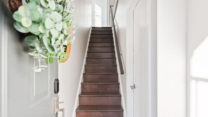 Un escalier en bois avec une rampe métallique, des murs blancs et une plante suspendue sur le côté gauche.