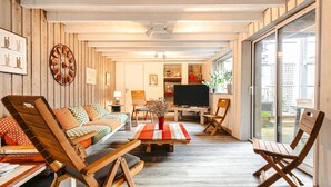A living room with a sofa, chairs, a coffee table, a TV, and a large window. - Holiday Home 'Couleur Patio, Loft Atypique, Sauna' with Private Terrace, Balcony and Wi-Fi (Saint-Denis-d'Oléron)