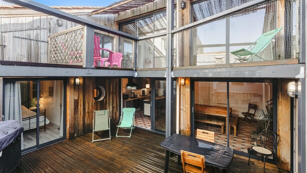 A multi-level outdoor space with a wooden deck, a dining area, and a kitchen visible through large windows. - Holiday Home 'Couleur Patio, Loft Atypique, Sauna' with Private Terrace, Balcony and Wi-Fi (Saint-Denis-d'Oléron)