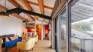 A modern interior with wooden beams, a blue sofa, yellow armchairs, and a large sliding glass door. - Holiday Home 'Couleur Patio, Loft Atypique, Sauna' with Private Terrace, Balcony and Wi-Fi (Saint-Denis-d'Oléron)