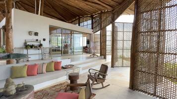 A spacious living area with a high ceiling, a sofa set, a rocking chair, and a dining table.