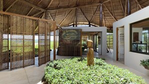 Um interior espaçoso com teto alto, divisórias de bambu e uma escultura central.