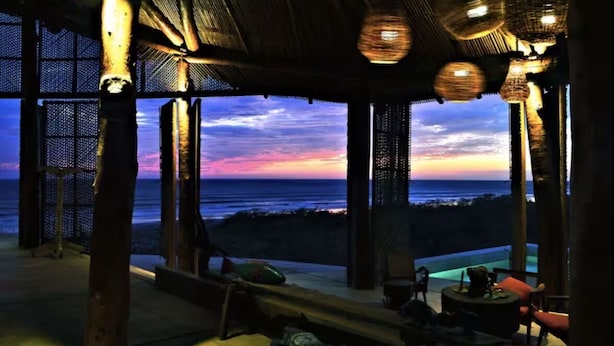Uma área de estar coberta ao ar livre com vista para o oceano ao pôr do sol.