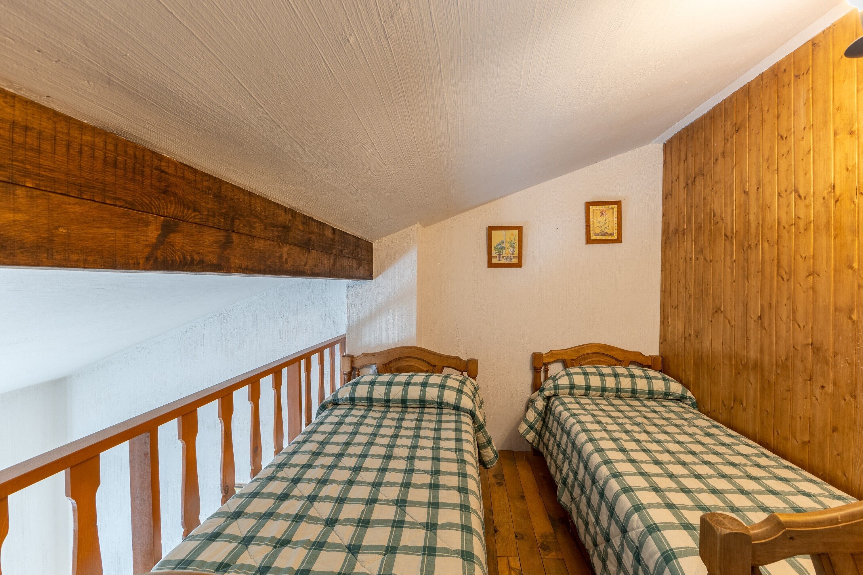 Una habitación con dos camas, paredes y escalera de madera, y un cuadro enmarcado en la pared.