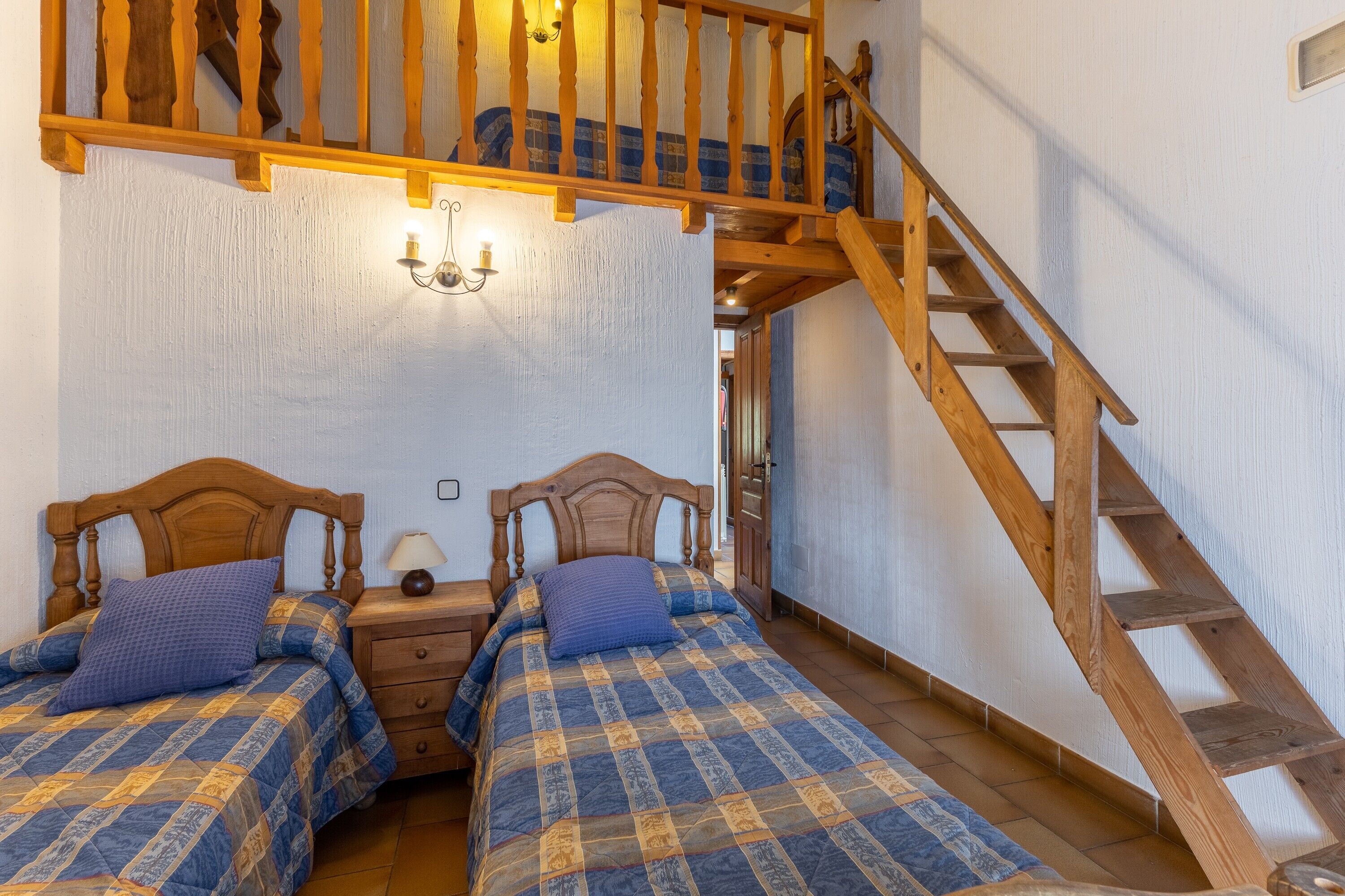 Un dormitorio con dos camas de madera, una mesita de noche, una lámpara y una escalera de madera.
