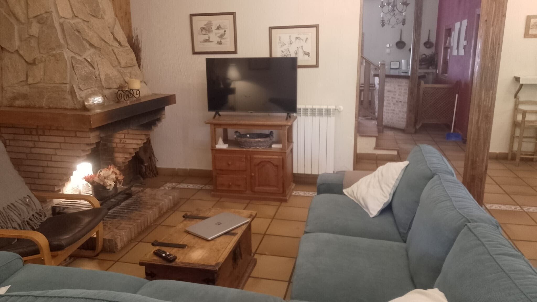 Una sala de estar con chimenea de piedra, un televisor sobre un soporte de madera, un sofá y una mesa de centro.