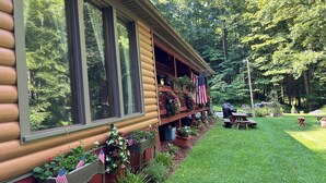 Une cabane en rondins dotée de grandes fenêtres, d’un porche orné de drapeaux américains et d’une table de pique-nique dans la cour.