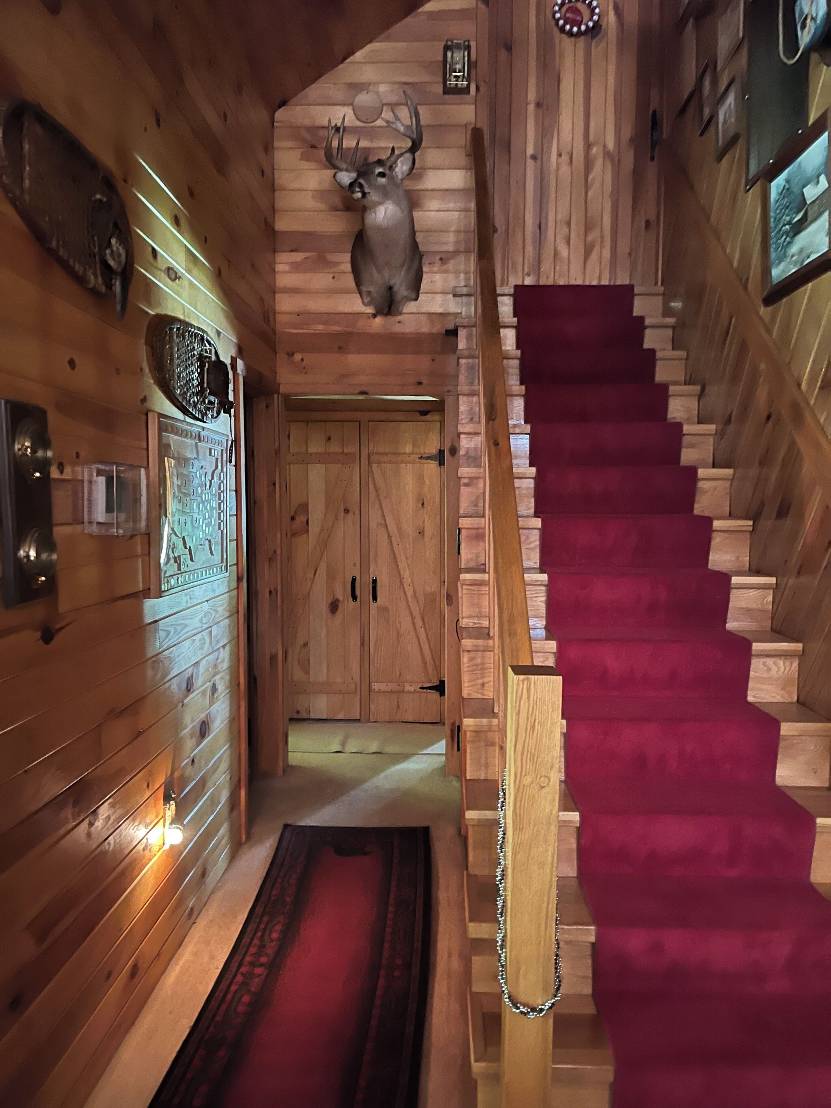A wooden interior with a staircase, wooden doors, and a mounted deer head.