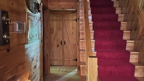 Un intérieur en bois avec un escalier, des portes en bois et une tête de cerf fixée au mur.
