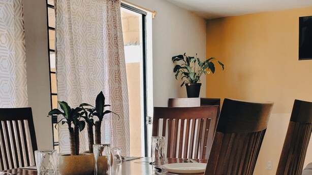 Zona pranzo con tavolo in legno apparecchiata per quattro persone, circondata da sedie imbottite.