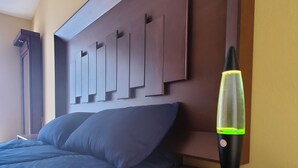 Una camera da letto con una testiera in legno, un letto con biancheria blu, un comodino con una lampada lava e un comò in legno.