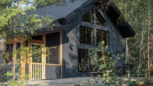 En moderne træhytte med store vinduer, en balkon og en træterrasse.