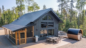 En hytte med stor terrasse, grill og en tøndestue.