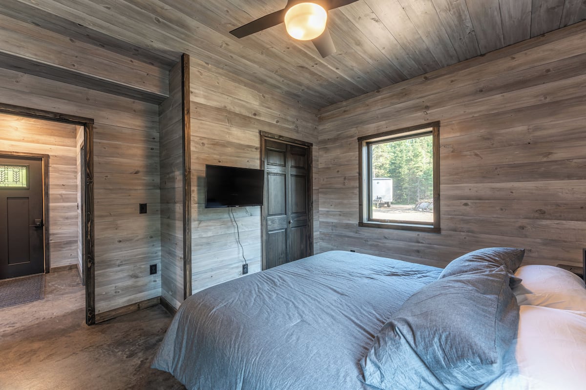 A bedroom with a bed, a television mounted on the wall, and a window providing natural light.