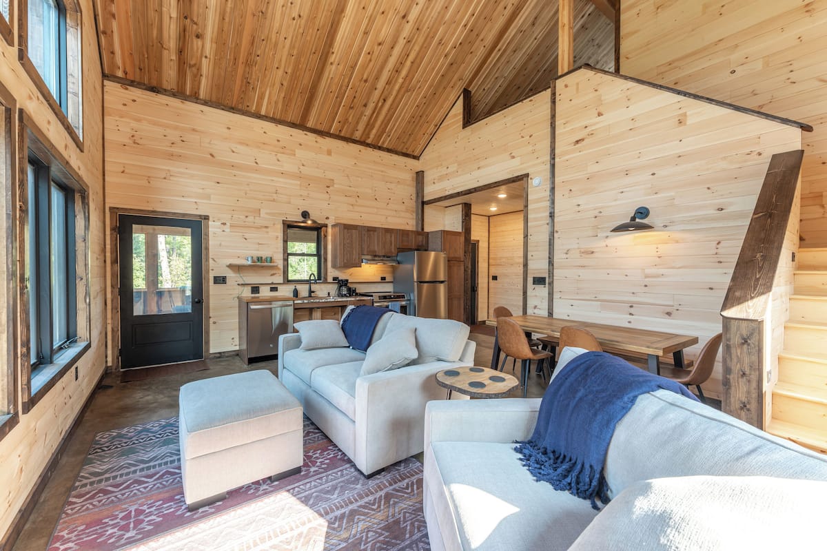A log cabin interior with a living area featuring sofas, a coffee table, and a dining table.