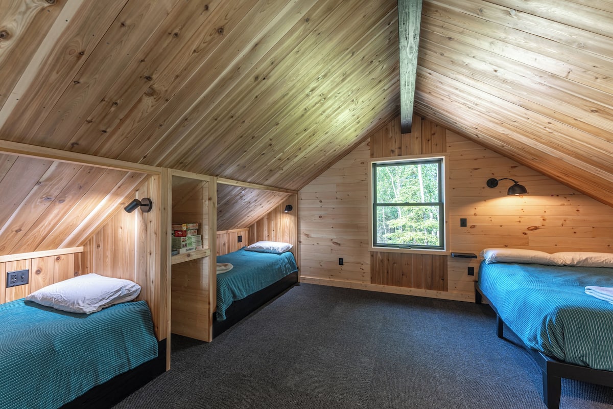 A cabin with two bedrooms, each with a bed and a window. The cabin has wooden walls and a sloped ceiling.
