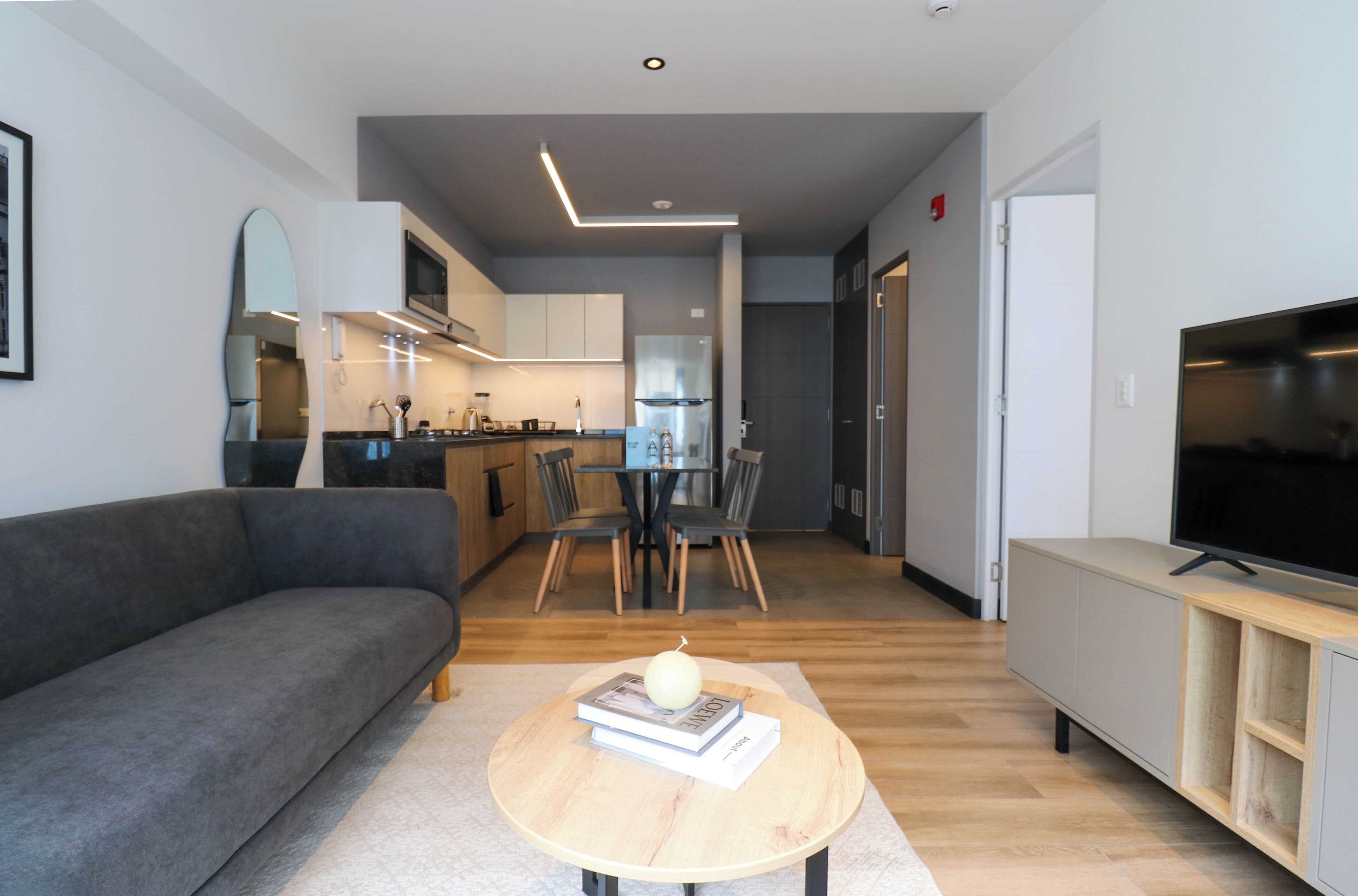 A modern living room with a grey sofa, a round wooden coffee table with books and a pear, and a TV on a wooden stand.