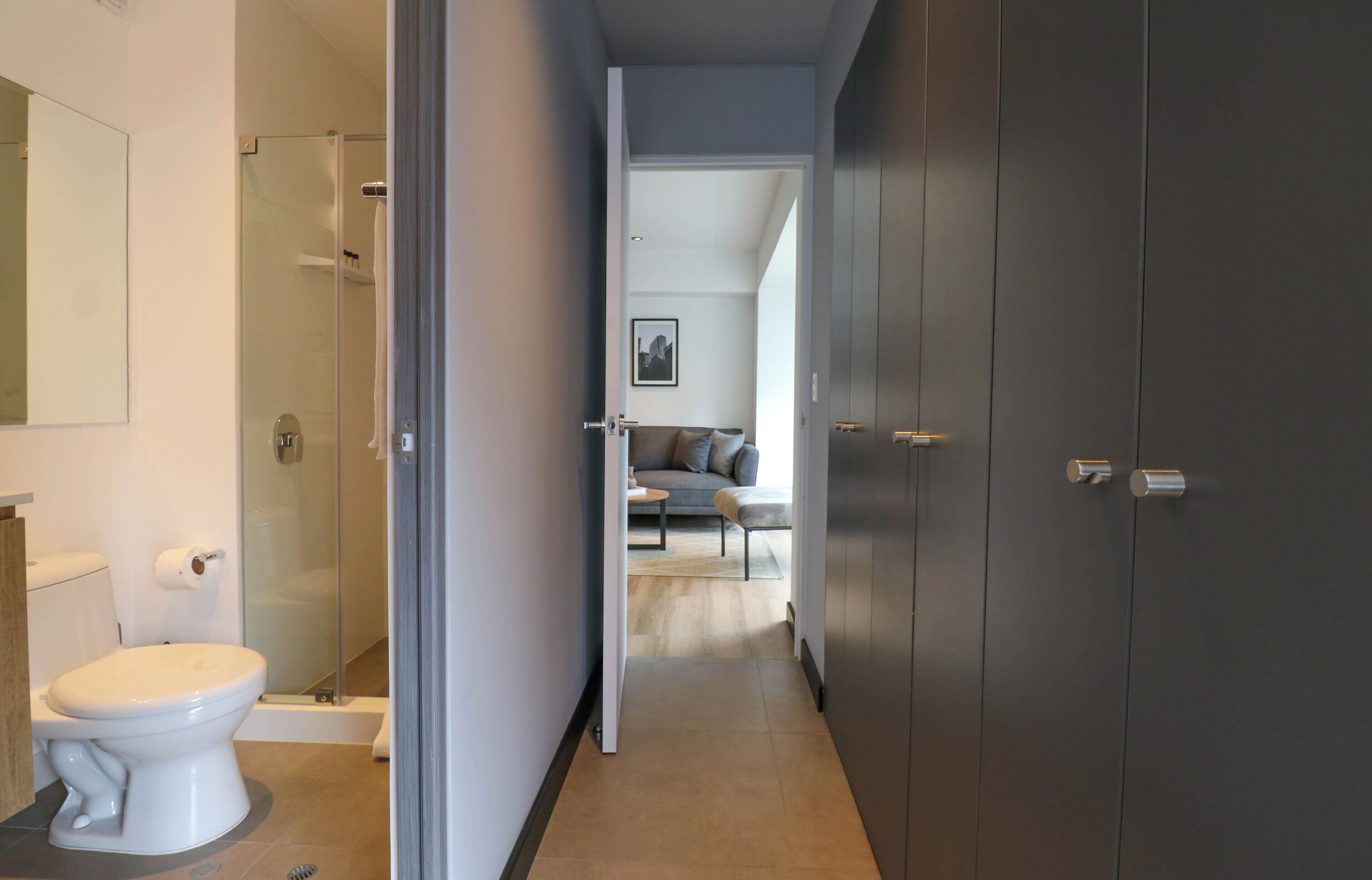 Un baño moderno con inodoro, ducha y puerta de cristal que da a una sala de estar con sofá y mesa de centro.