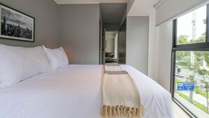 A hotel room with a large bed, a cityscape view through the window, and a framed picture on the wall. - Arona by Wynwood House (Lima)