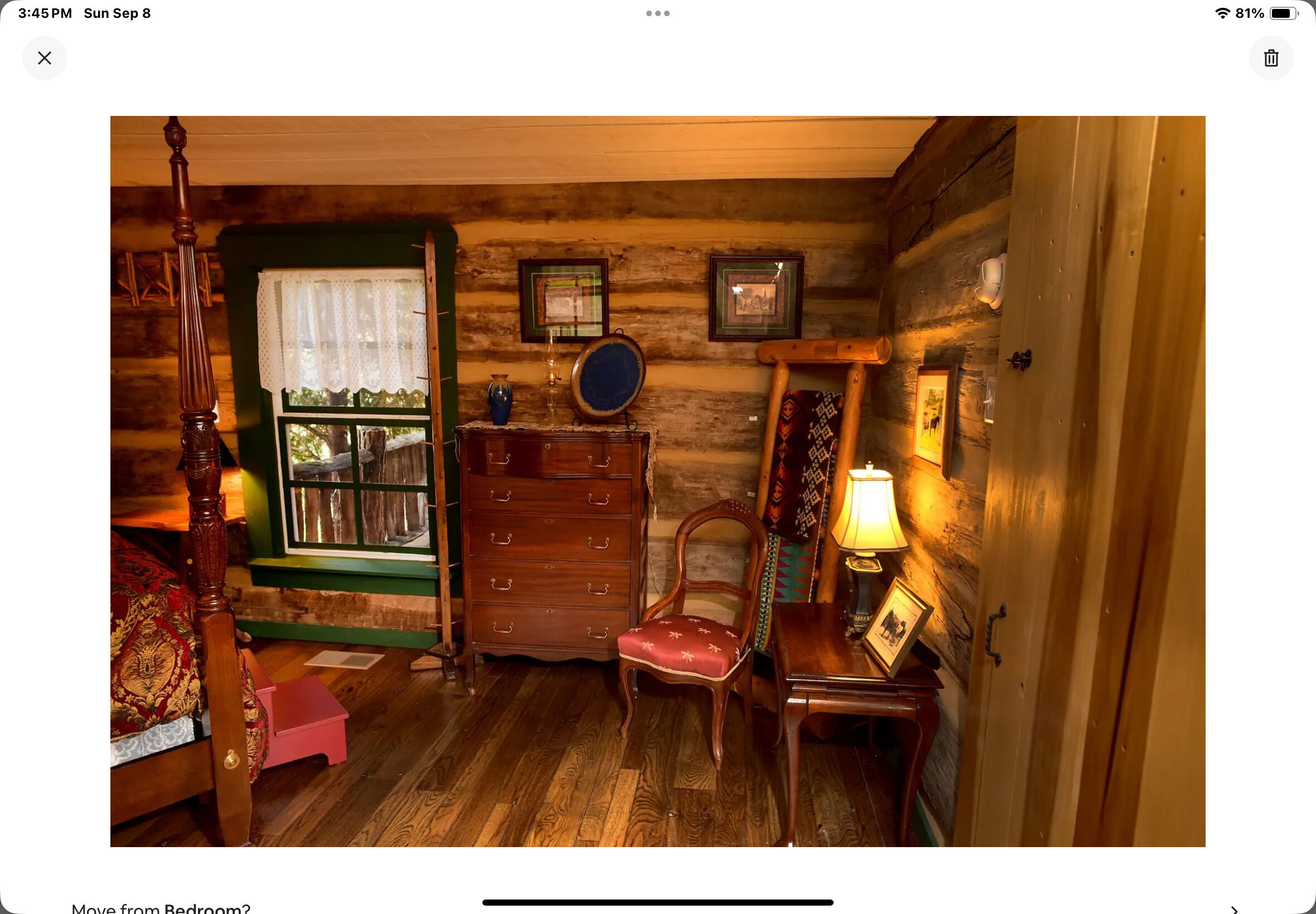 Ein gemütliches Schlafzimmer in einer Blockhütte mit einem hölzernen Bett, einem Schminktisch, einem Sessel und einem kleinen Tisch mit einer Lampe.
