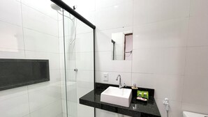 Un bagno moderno con doccia vetrata, lavandino bianco e piano di appoggio nero, e un water.