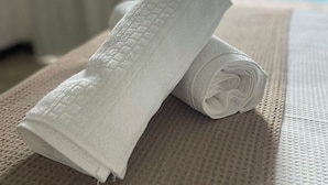 Un asciugamano bianco arrotolato su un tappetino beige strutturato, con una piscina sullo sfondo.