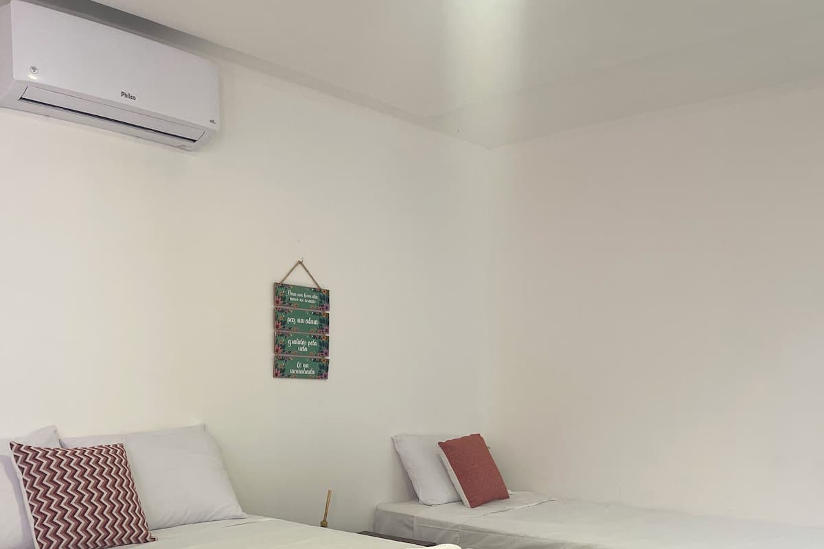 Habitación de hotel con dos camas, una manta verde azulada en la cama de la izquierda y un aire acondicionado de pared.