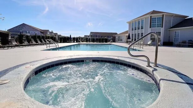 A swimming pool with a hot tub in the center, surrounded by lounge chairs and a building with large windows.