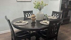 A dining area with a round table, black chairs, a vase with flowers, and framed artwork on the wall.