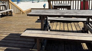 A wooden deck with picnic tables overlooking a beach.