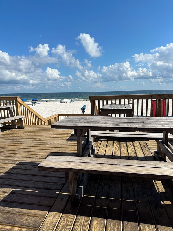 Terraza de madera con mesas de picnic con vistas a una playa.