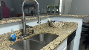 A kitchen with granite countertops, stainless steel sink, white cabinets, and a dishwasher.