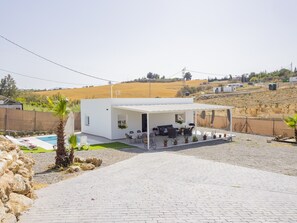 Uma casa moderna com varanda coberta, piscina e vista para uma paisagem montanhosa.