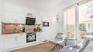 A modern kitchen with white cabinets, a microwave, an oven, and a glass dining table with chairs. - "Kuschelnest" Vacation Home: Modernly Furnished with a Sun Terrace - Cozy (Kamminke)